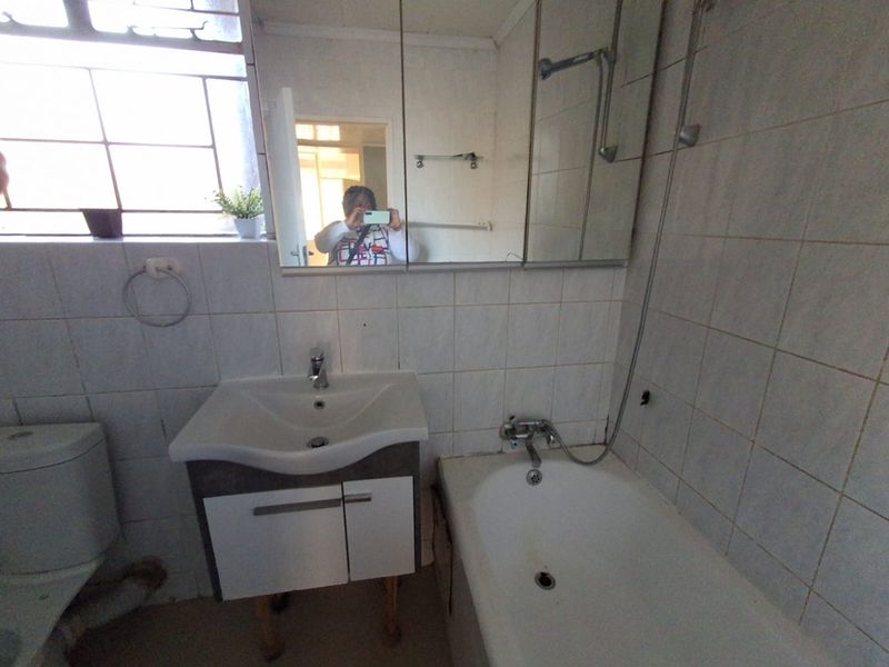 A dated bathroom featuring a vanity unit, bathtub with shower attachment, and tiled walls. The space requires cosmetic updates to improve its overall condition.