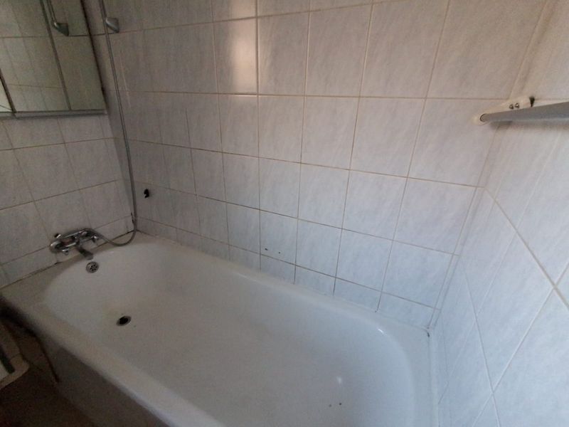 A functional bathroom featuring a standard bathtub with shower mixer, tiled walls, and a built-in medicine cabinet.