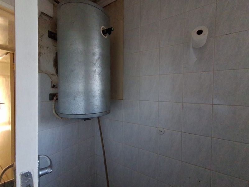 A bathroom space featuring a wall-mounted electric water heater and tiled walls, currently requiring maintenance and repair to the surrounding wall finishes.