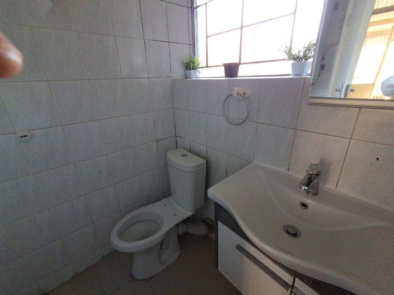A compact bathroom featuring a vanity basin, toilet, and tiled walls. The space requires some maintenance and cosmetic updates to improve its overall condition.