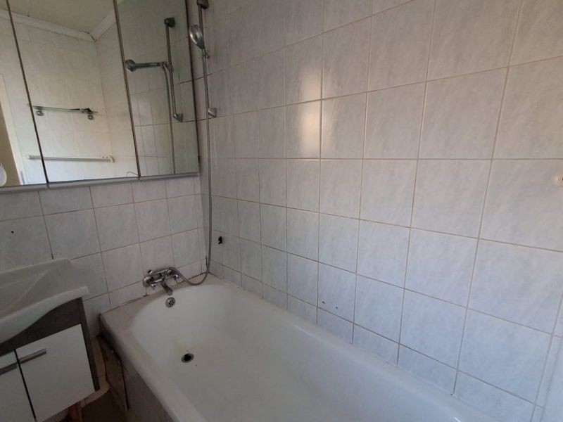 A dated bathroom featuring a standard bathtub with shower mixer, wall-mounted mirror cabinet, and vanity basin with tiled wall finishes.