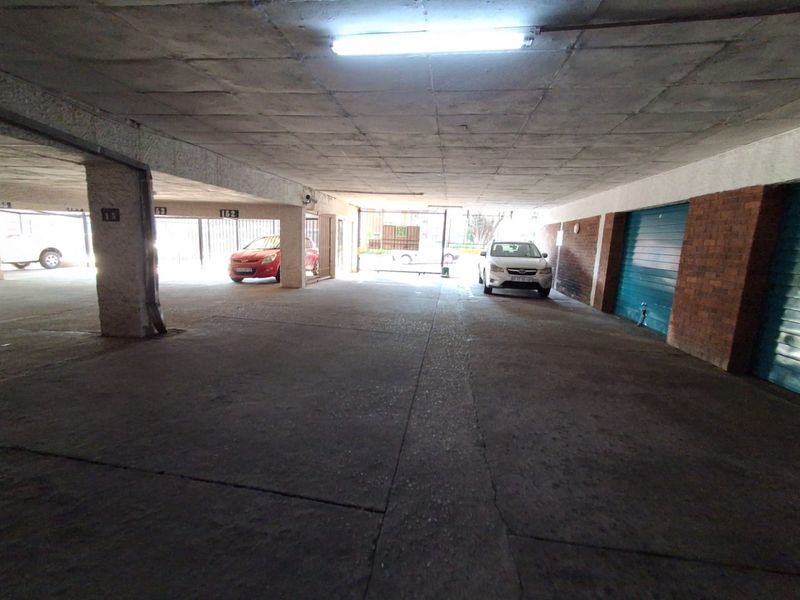 A covered parking garage area featuring concrete flooring, exposed concrete ceilings, and secure metal gate access.