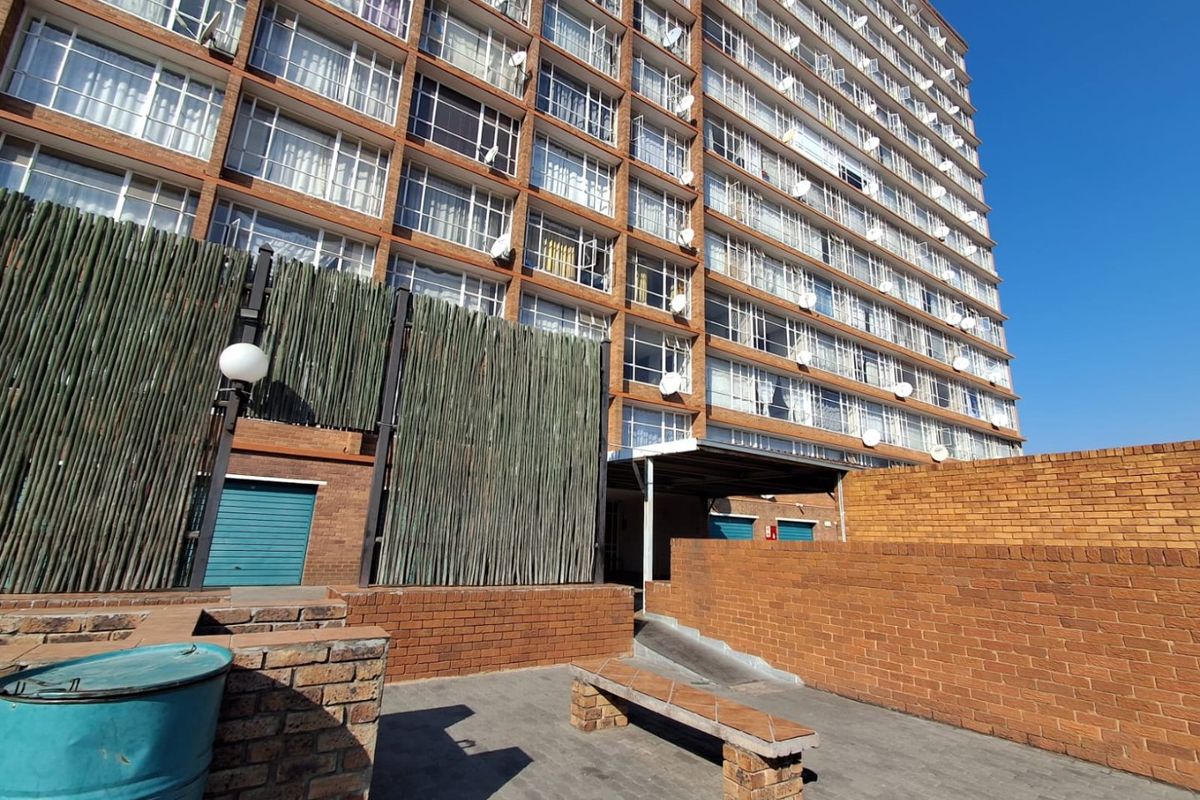 Exterior view of the apartment building rear courtyard featuring brick facade, paved ground, and ramp access to the building entrance.