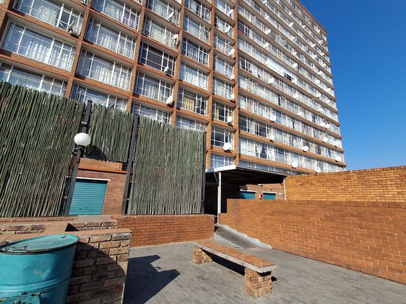 Exterior view of the apartment building rear courtyard featuring brick facade, paved ground, and ramp access to the building entrance.
