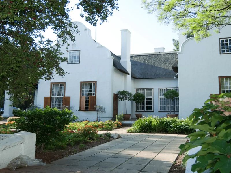 A well-maintained commercial property featuring traditional Cape Dutch architecture with a thatched roof, gabled facade, and paved garden walkway.