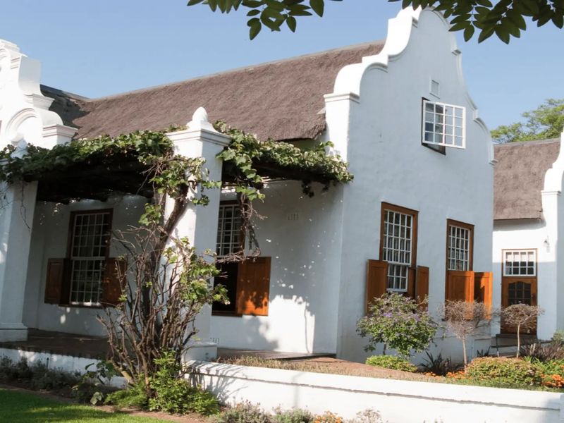 A charming commercial property featuring traditional Cape Dutch architecture with a thatched roof, white gabled facade, and a welcoming covered veranda.