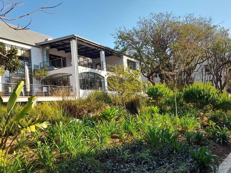 Rear view of a commercial building featuring multi-level balconies, large windows, and well-maintained landscaped gardens with paved walkways.