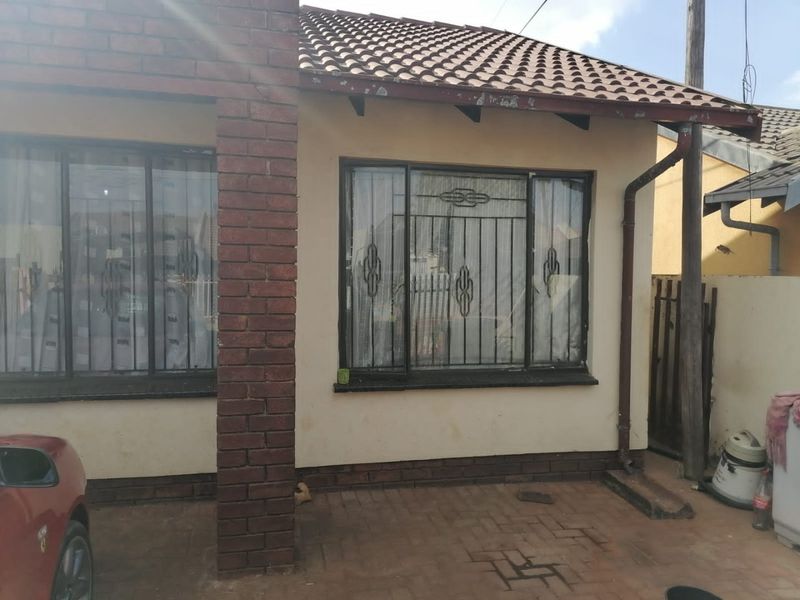 Front elevation of a brick-built house featuring tiled roofing, security bars on windows, and a paved driveway area.