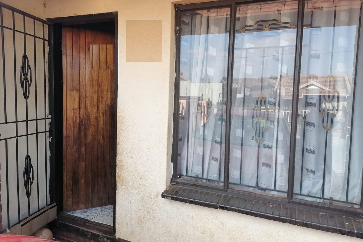 Front entrance view showing a timber door with a security gate and a metal-framed window with a brick sill.
