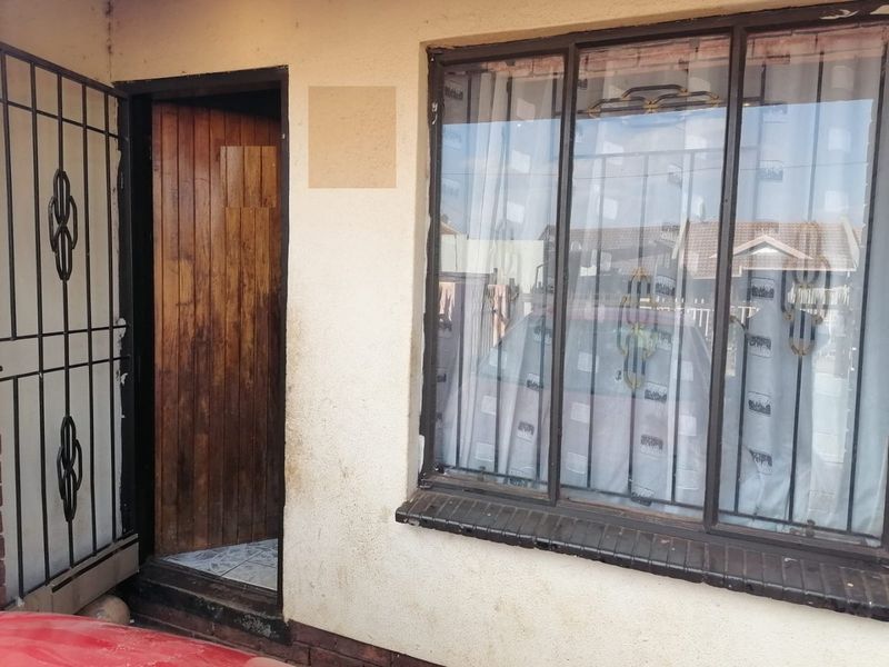Front entrance view showing a timber door with a security gate and a metal-framed window with a brick sill.