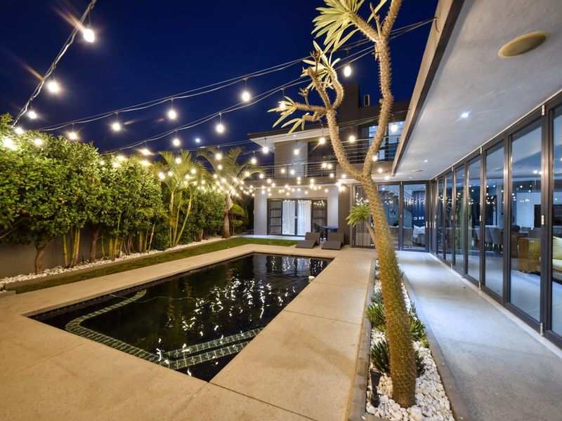 A beautifully illuminated outdoor pool area featuring a modern swimming pool, paved patio, and seamless indoor-outdoor flow through large bi-fold doors.