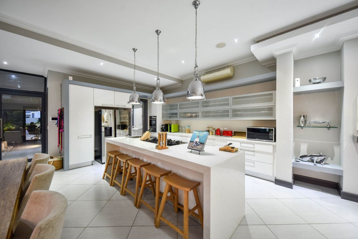 Modern kitchen featuring a large central island with quartz countertops, built-in appliances, sleek cabinetry, and stylish pendant lighting in an open-plan layout.