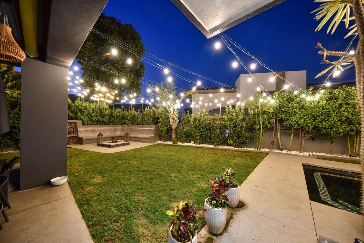 A beautifully landscaped rear garden featuring a built-in concrete bench, fire pit, and atmospheric string lighting, perfect for outdoor entertaining.