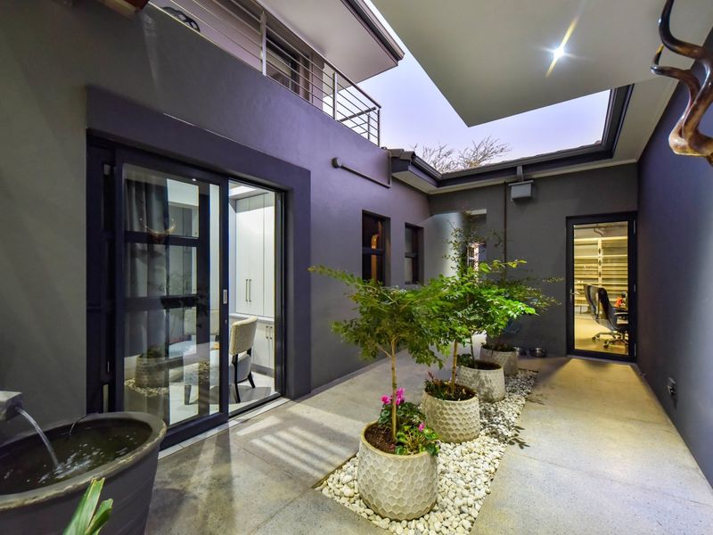 A modern, well-maintained courtyard patio featuring a stone pebble garden bed, water feature, and seamless access to interior living spaces through sliding glass doors.