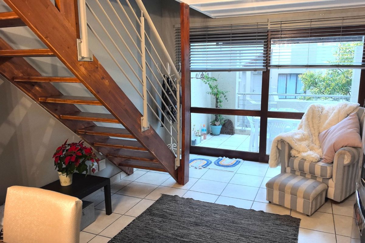 Living area featuring a wooden staircase with metal balustrade, tiled flooring, and large sliding glass doors leading to an outdoor patio space.
