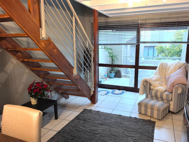 Living area featuring a wooden staircase with metal balustrade, tiled flooring, and large sliding glass doors leading to an outdoor patio space.