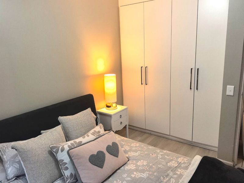 A well-maintained bedroom featuring neutral walls, light laminate flooring, and a large white built-in wardrobe with modern handles.