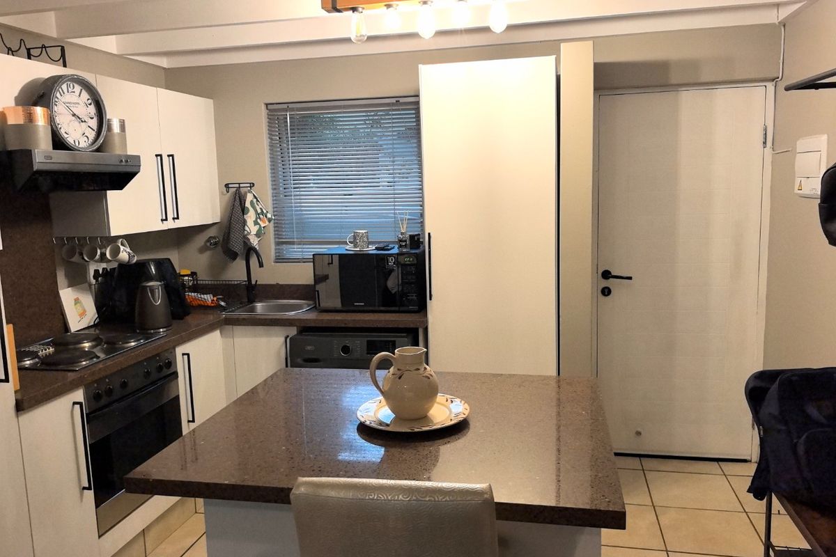 A functional kitchen featuring stone countertops, built-in oven and hob, central island, and ample cabinetry, finished with neutral tones and tiled flooring.