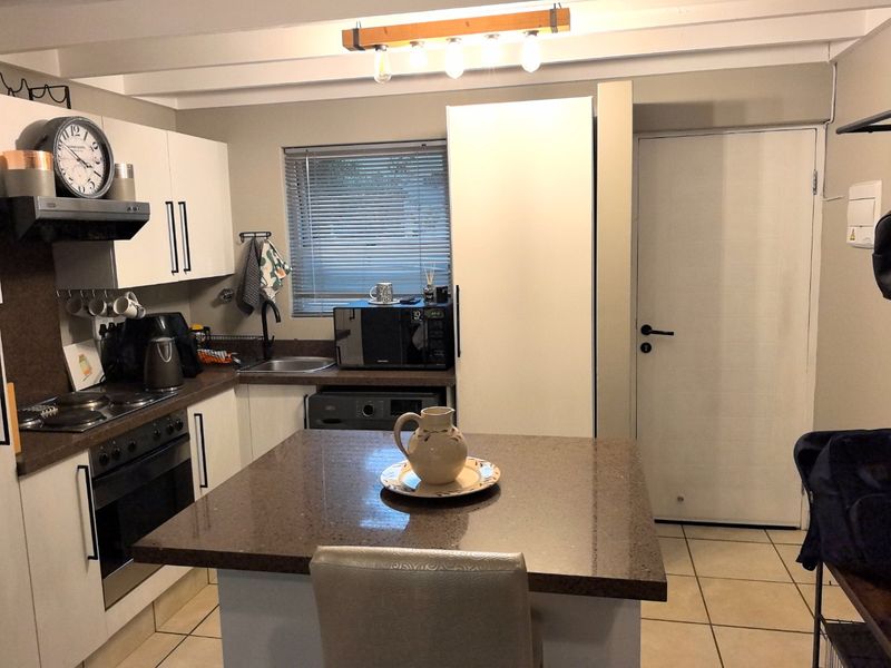 A functional kitchen featuring stone countertops, built-in oven and hob, central island, and ample cabinetry, finished with neutral tones and tiled flooring.