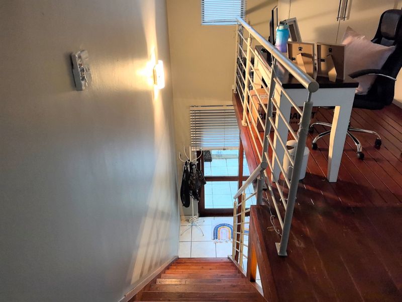 A view looking down a wooden staircase towards the entrance, featuring a mezzanine level with a metal balustrade and tiled flooring.