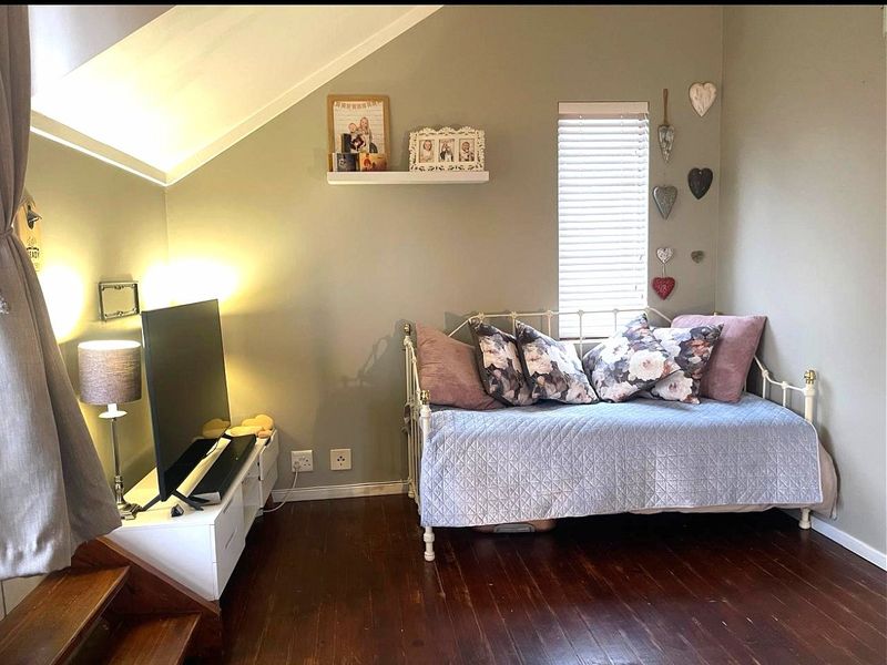 A cozy bedroom featuring dark timber flooring, a sloped ceiling, and a window fitted with venetian blinds.