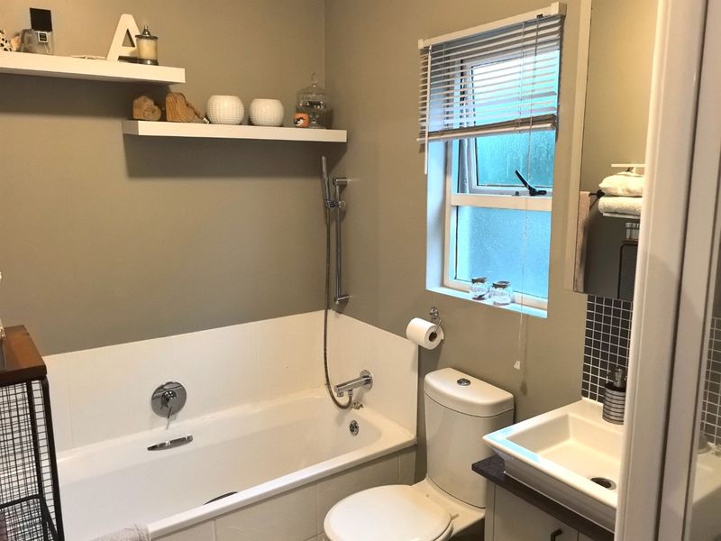 A functional bathroom featuring a bathtub with handheld shower, a modern vanity basin, toilet, and convenient floating wall shelves for storage.