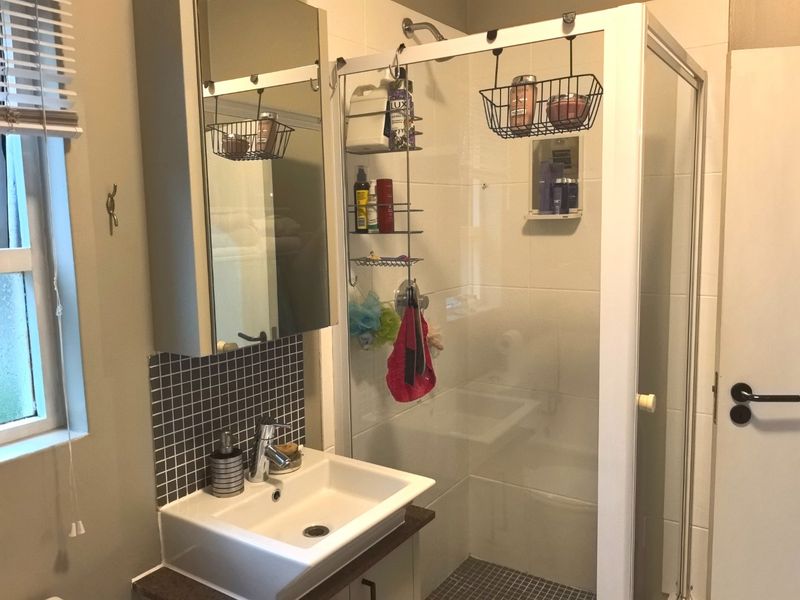 A functional bathroom featuring a glass shower enclosure, a modern vanity basin with a mosaic tile splashback, and a mirrored medicine cabinet.