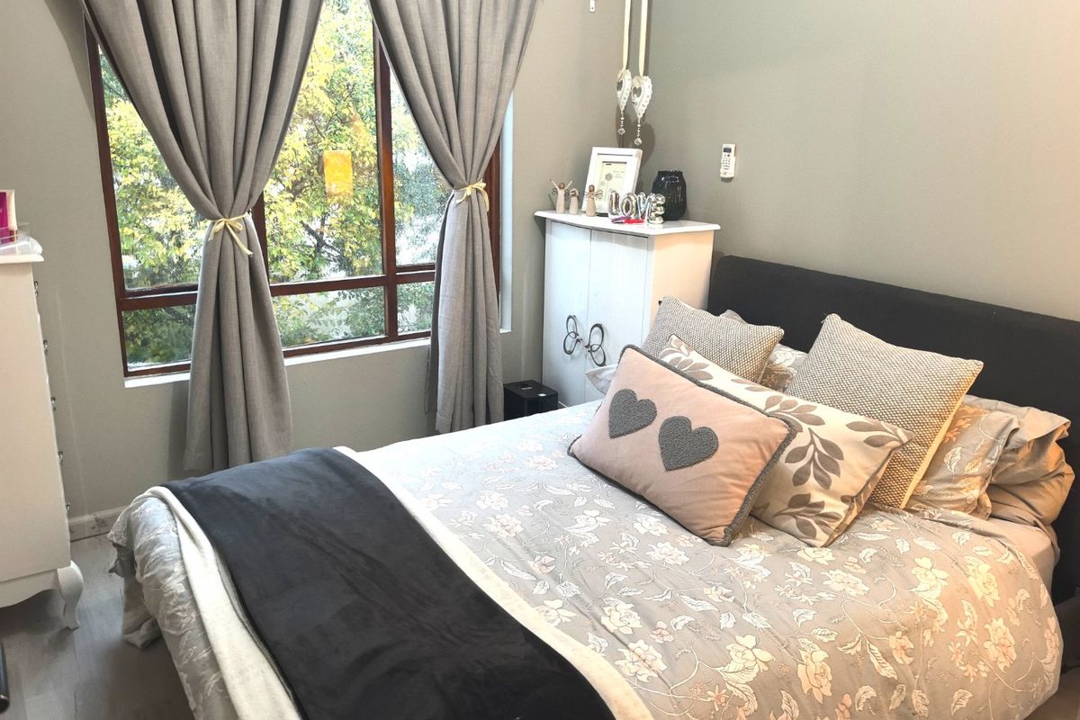 A well-lit bedroom featuring neutral wall tones, laminate flooring, and a large window providing natural light and a pleasant outdoor view.