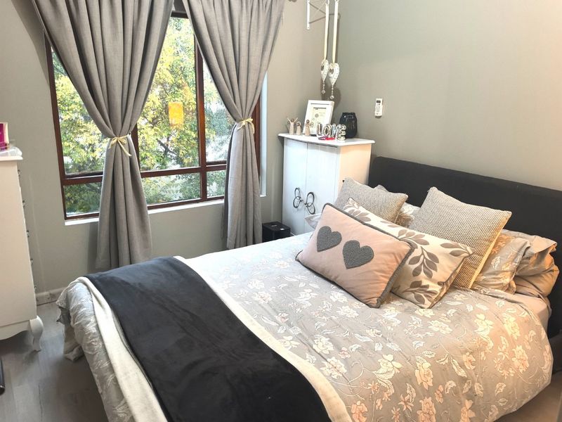 A well-lit bedroom featuring neutral wall tones, laminate flooring, and a large window providing natural light and a pleasant outdoor view.