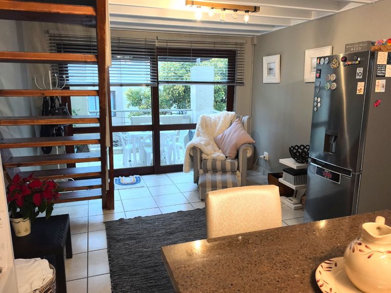 Open plan living area featuring tiled floors, exposed ceiling beams, a wooden staircase, and sliding glass doors leading to an outdoor balcony.