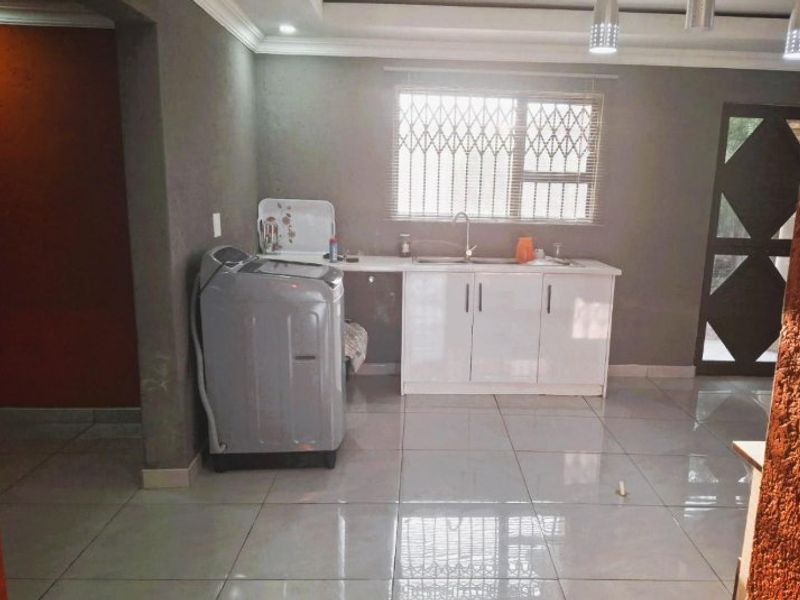 A functional laundry area featuring tiled flooring, built-in white cabinetry with a stainless steel sink, and secure window bars.