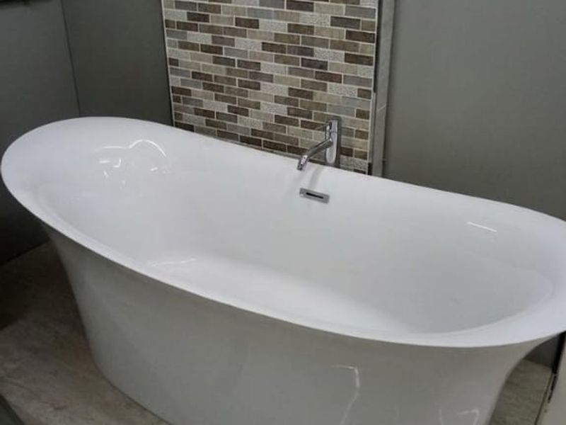 A modern bathroom featuring a sleek freestanding bathtub set against a decorative mosaic tile feature wall on a raised tiled platform.