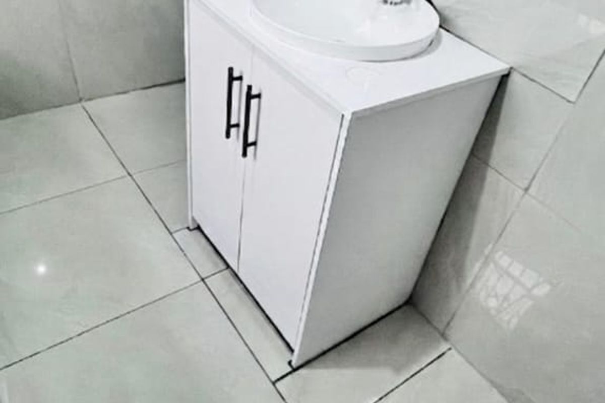 A compact bathroom featuring a modern white vanity cabinet with a vessel sink and neutral wall and floor tiling.
