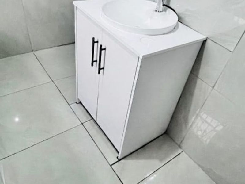 A compact bathroom featuring a modern white vanity cabinet with a vessel sink and neutral wall and floor tiling.