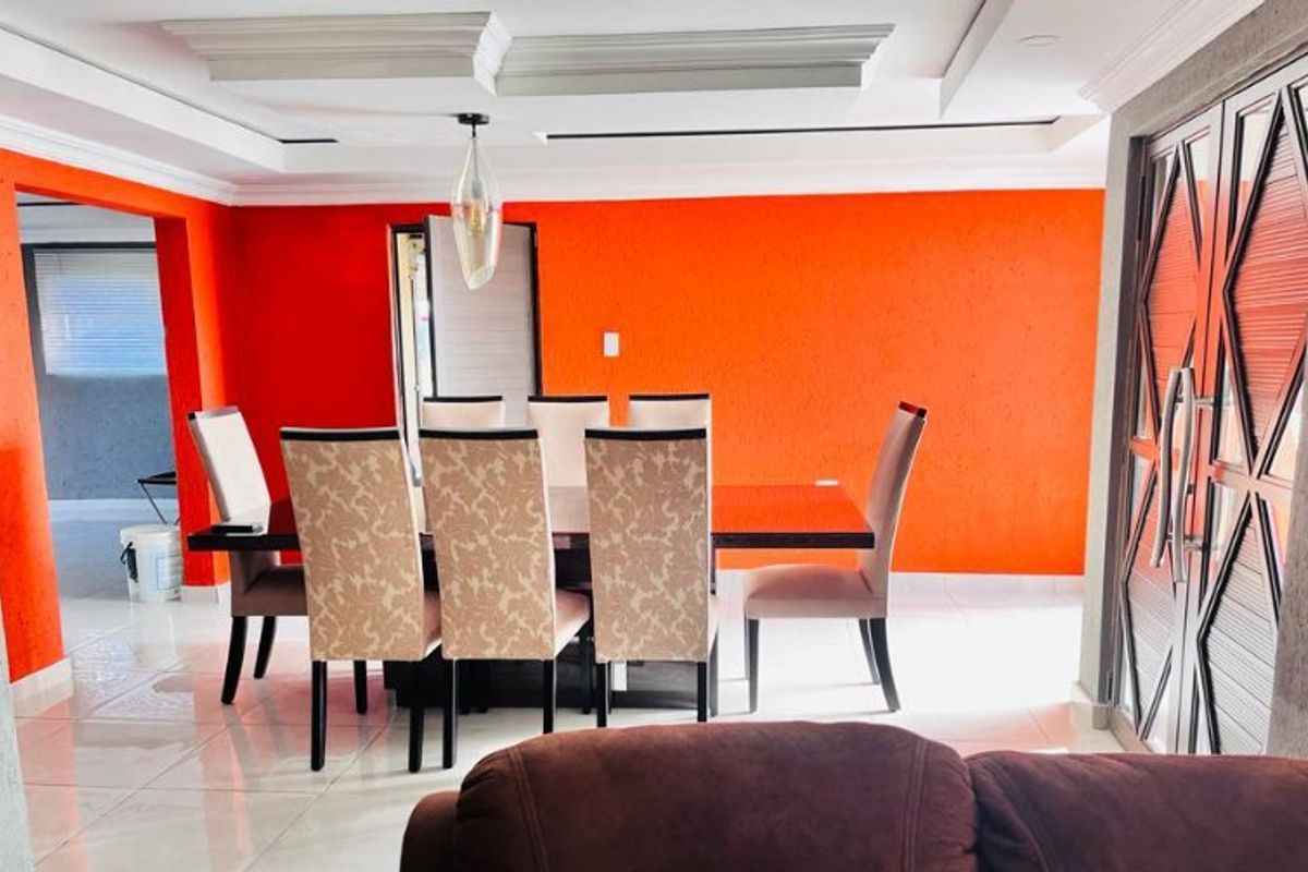 Dining room featuring bright orange accent walls, recessed ceiling with cove lighting, and polished tile flooring, providing a vibrant space for meals.