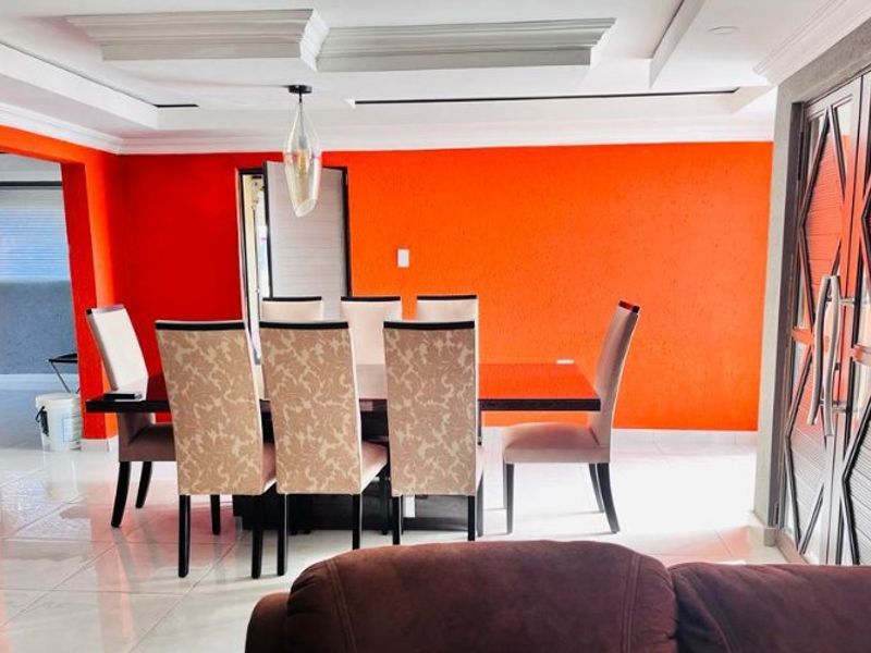 Dining room featuring bright orange accent walls, recessed ceiling with cove lighting, and polished tile flooring, providing a vibrant space for meals.