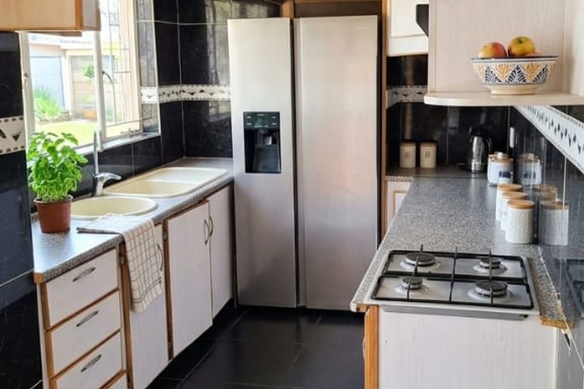 A functional galley-style kitchen featuring dark tiled flooring, a gas hob, double sink, and ample built-in cabinetry with a contrasting tiled backsplash.