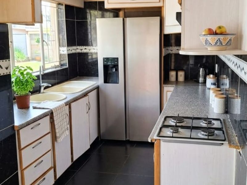 A functional galley-style kitchen featuring dark tiled flooring, a gas hob, double sink, and ample built-in cabinetry with a contrasting tiled backsplash.