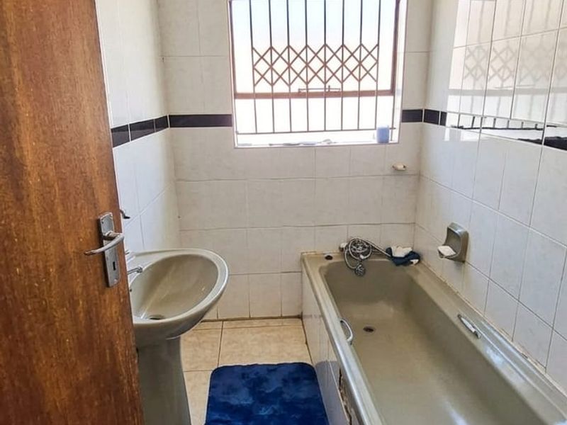 A compact bathroom featuring a pedestal basin, built-in bathtub, and tiled finishes, requiring modernization to update the dated sanitaryware.