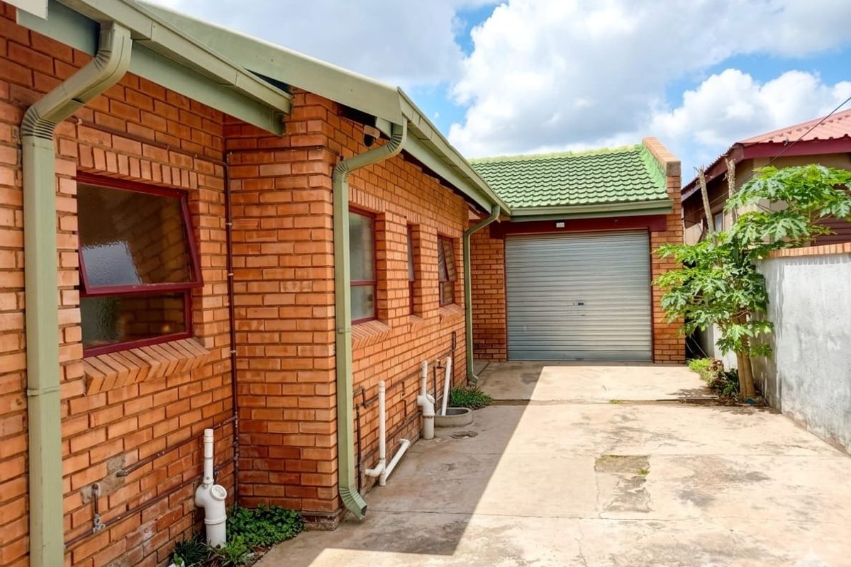 Rear exterior view of the property featuring a face brick facade, concrete driveway, and a secure roller shutter garage door.