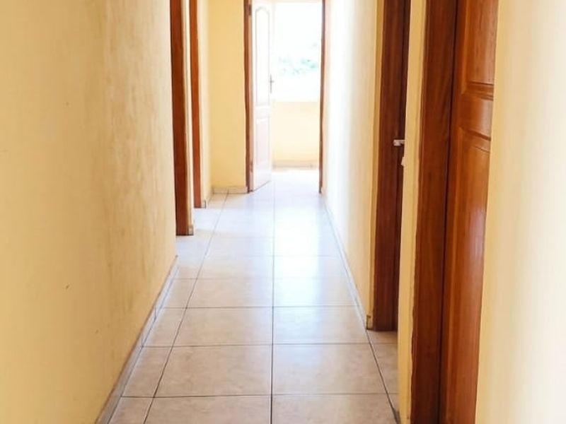 A bright, tiled hallway featuring wooden doors and a skylight, providing access to multiple rooms within the home.
