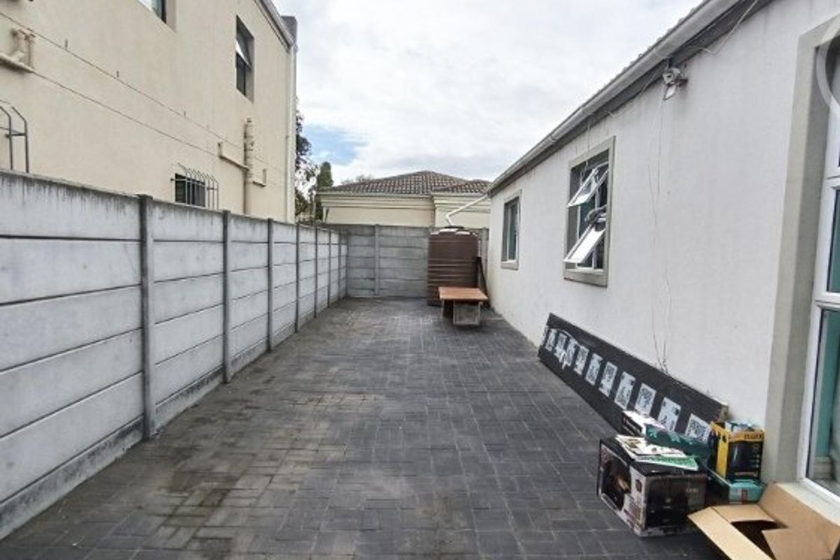 A paved rear courtyard area enclosed by precast concrete boundary walls, featuring a water tank and direct access to the side of the house.