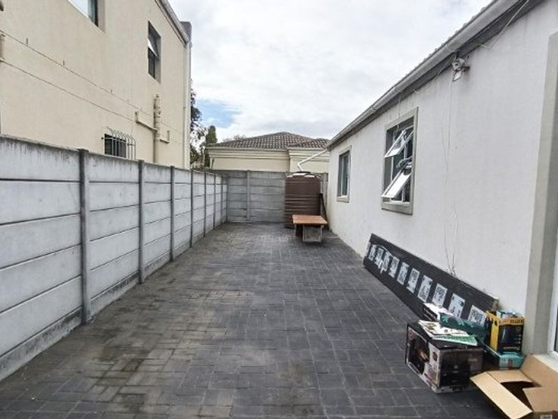 A paved rear courtyard area enclosed by precast concrete boundary walls, featuring a water tank and direct access to the side of the house.