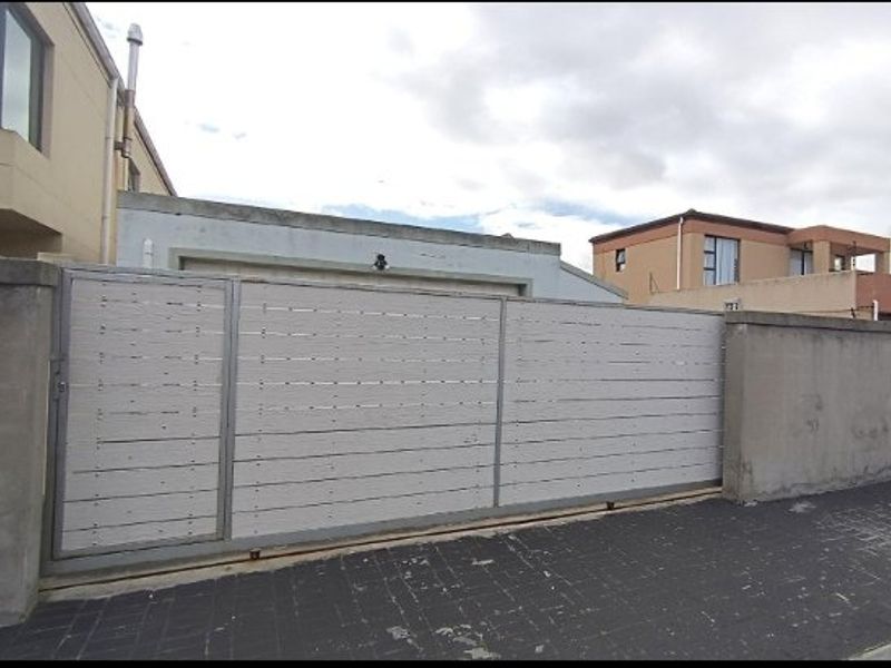 Front exterior view of the property featuring a modern horizontal slat sliding gate, concrete boundary wall, and paved driveway access to the garage.