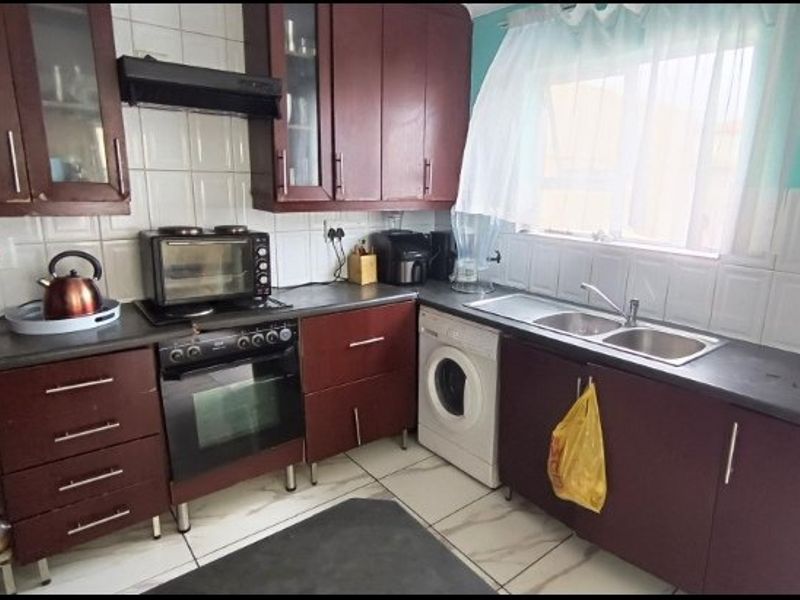 A functional kitchen featuring dark wood-toned cabinetry, tiled backsplash, integrated oven with extractor fan, and a double bowl sink with tiled flooring.
