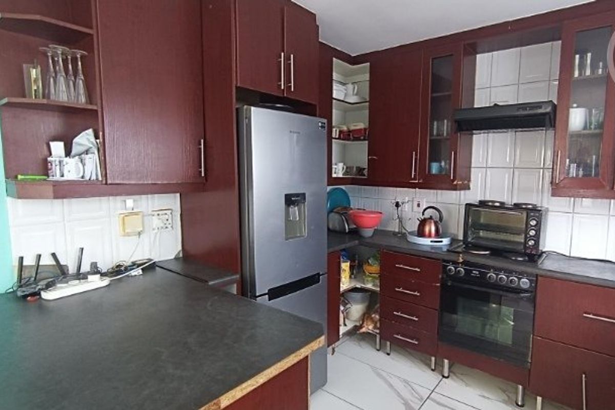 A functional kitchen featuring dark wood cabinetry, tiled backsplash, built-in oven with extractor fan, and marble-look floor tiles.