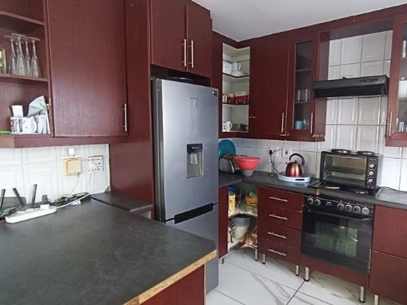 A functional kitchen featuring dark wood cabinetry, tiled backsplash, built-in oven with extractor fan, and marble-look floor tiles.