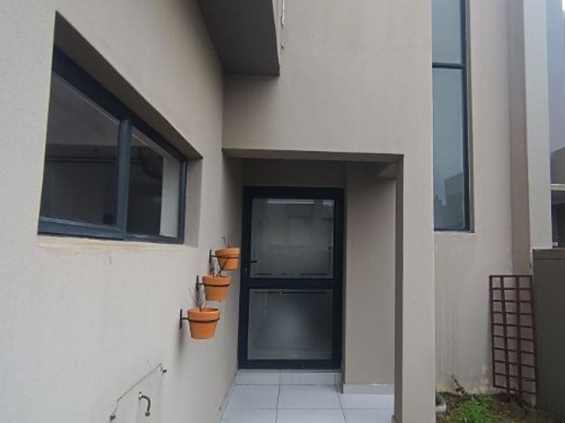 Modern front entrance featuring a glass panel door, tiled flooring, and dark aluminium window frames with a neutral exterior facade.