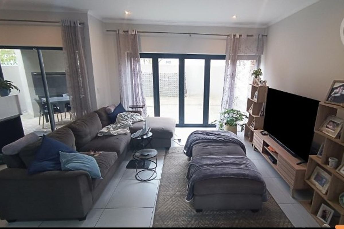 A bright living room featuring large bi-fold doors that open to an outdoor patio area, complemented by neutral tiled flooring and recessed lighting.