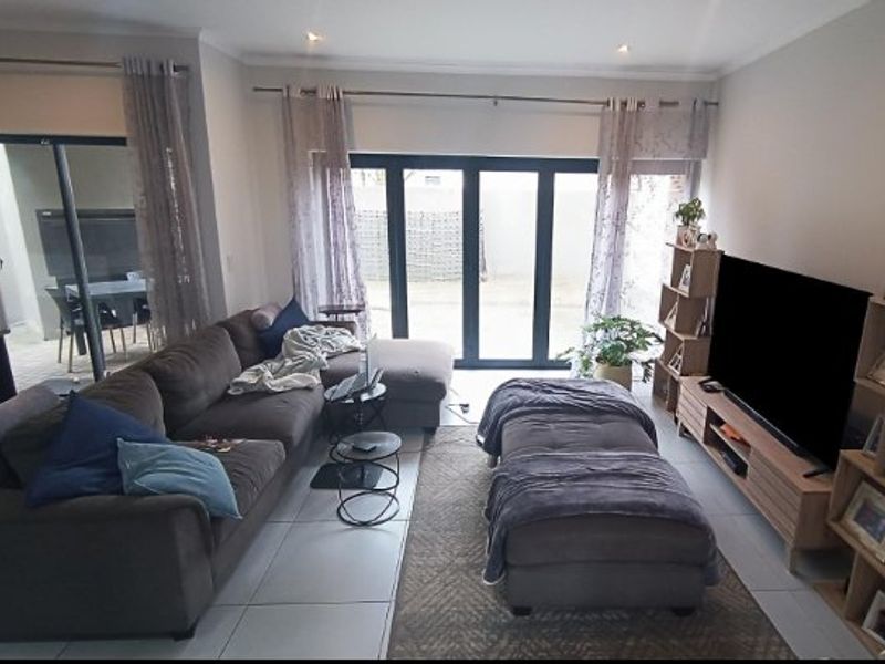 A bright living room featuring large bi-fold doors that open to an outdoor patio area, complemented by neutral tiled flooring and recessed lighting.